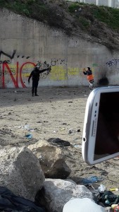A French officer aims a teargas canister at a refugee with his hands in the air.